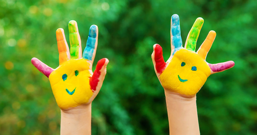 photo of young child's hands covered in a colorfully painted smiley face